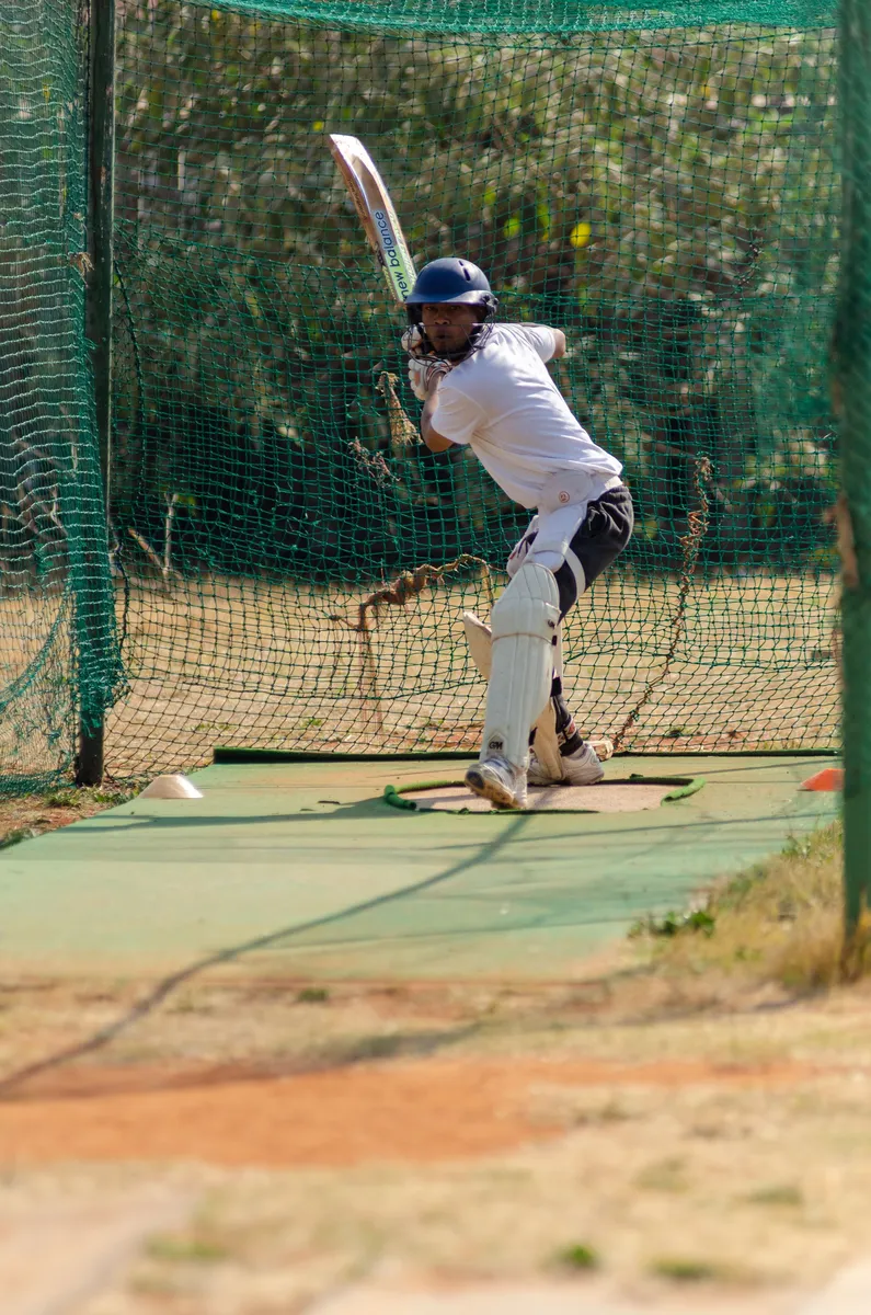 Batter taking guard inside a cricket practice net lane at an outdoor ground