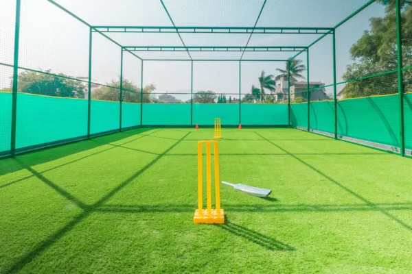 Cricket practice net cage with yellow stumps and a bat on artificial turf