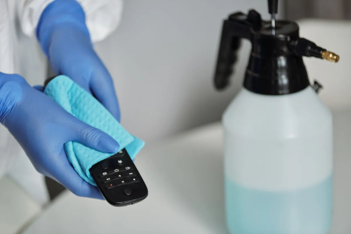 Gloved hand wiping a surface with a cloth next to a spray bottle