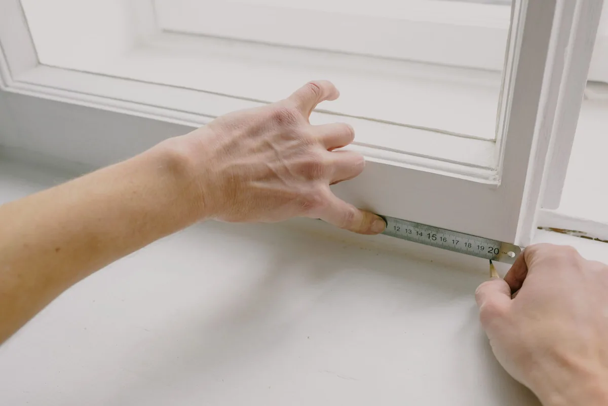 Hands measuring a window frame with a steel tape before ordering a mosquito net