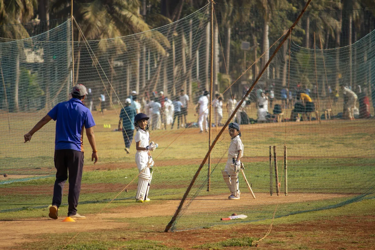 Several outdoor cricket practice net lanes at a ground with players training