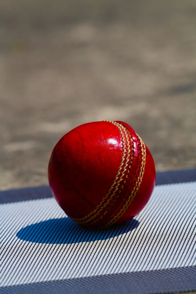 Red leather cricket ball resting on a mat, close-up