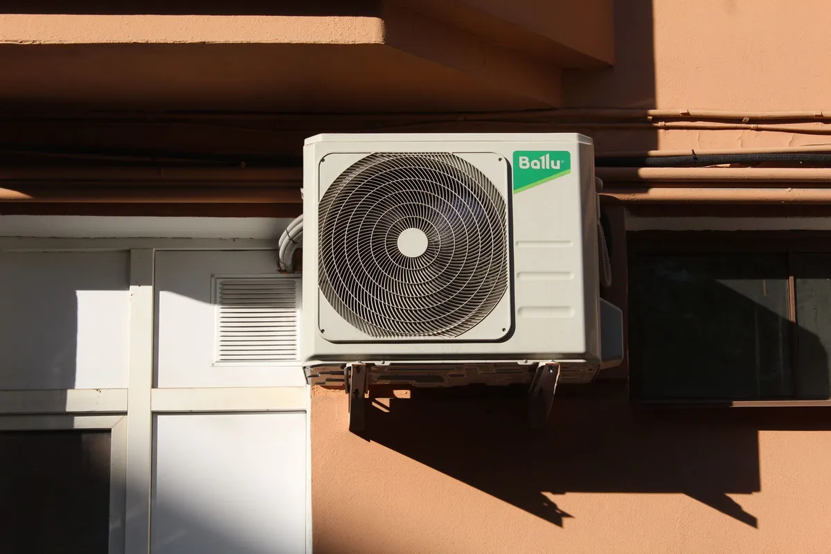 Split AC outdoor unit mounted on a wall bracket in bright sunlight
